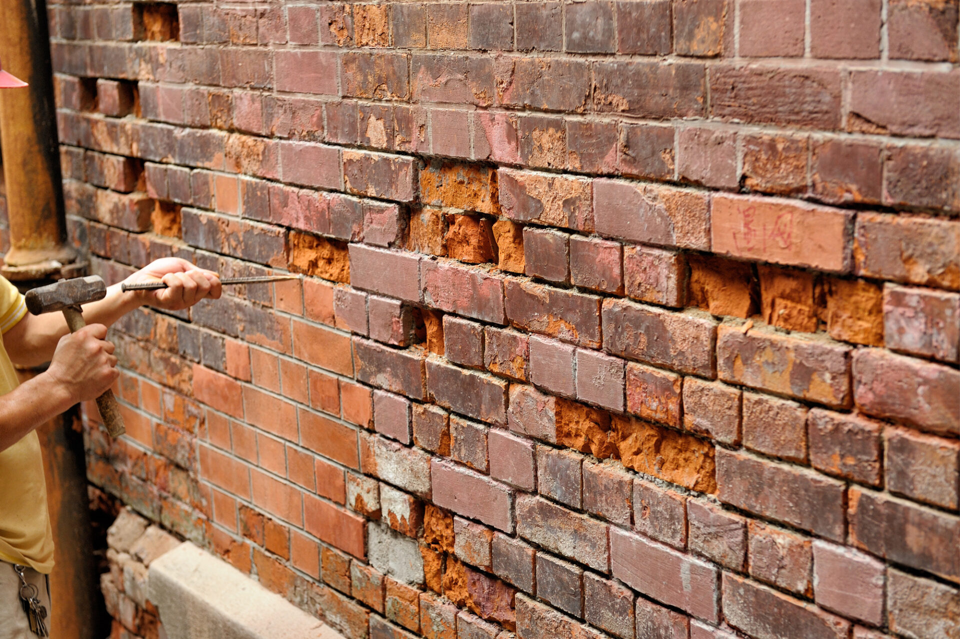 Repairing old brick wall using hammer and burin.